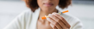 Cropped view of blurred african american businesswoman with diabetes holding syringe in office, banner  clipart