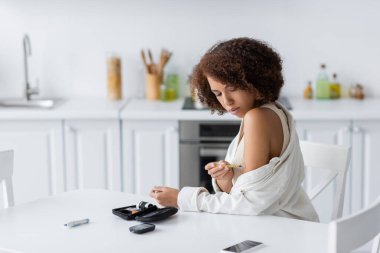 Diyabet hastası genç Afro-Amerikalı kadın tıbbi malzeme yanında insülin iğnesi yapıyor ve mutfakta akıllı telefon kullanıyor. 