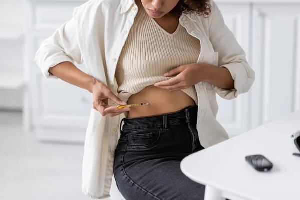 stock image Cropped view of african american woman doing insulin injection in belly near glucometer in kitchen 