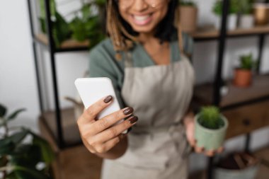 Çiçekçide videocuda elinde akıllı telefonla gülümseyen Afrikalı Amerikalı kadının kısmi görüntüsü