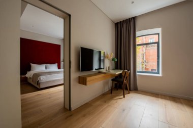 flat tv screen near desk and wooden chair next to bedroom in hotel room 