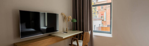 телевизор с плоским экраном рядом с деревянным столом и стулом в гостиничном номере, баннер 