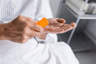 Cropped view of elderly patient holding pills in hospital ward clipart