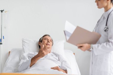 Yaşlı hasta hastane koğuşunda bulanık bir doktorla konuşuyor.