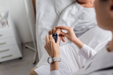 Klinikteki hastanın parmağına nabız oksimetresi takan doktor görüşü. 
