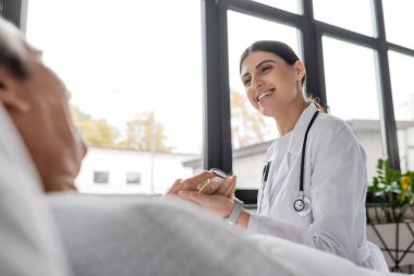 Klinikteki bulanık hastanın parmağına nabız oksimetresi takan neşeli doktor. 
