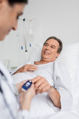 Nabız oksimetresi olan kıdemli bir hasta klinikteki bulanık doktora bakıyor. 