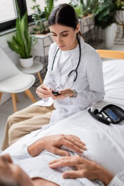 Klinikte yatağında yaşlı bir hastanın yanında glukometre tutan doktor. 