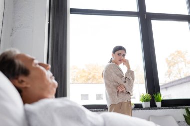 Üzgün kadın, klinikte yatakta yatan bulanık babaya bakıyor. 