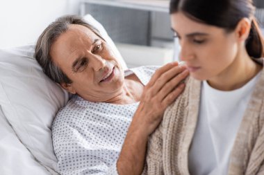 Gülümseyen kıdemli hasta klinikte bulanık kızını sakinleştiriyor. 