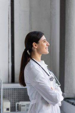 Side view of smiling doctor with stethoscope looking away in hospital ward  clipart