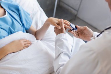 Klinikteki hastanın elinde nabız oksimetresi olan kıdemli doktorun görüntüsü. 