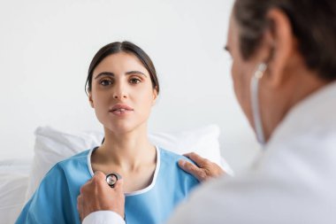Klinikteki hastanın göğsüne steteskop tutan bulanık bir doktor. 