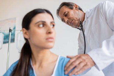 Steteskoplu kıdemli doktor klinikteki bulanık hastayı kontrol ediyor. 