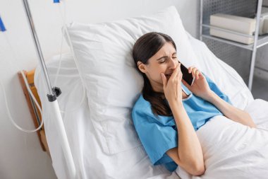 Hastanedeki yatakta akıllı telefonla konuşurken hoşnutsuz bir hastanın ağlayışını yüksek açıdan görmek. 
