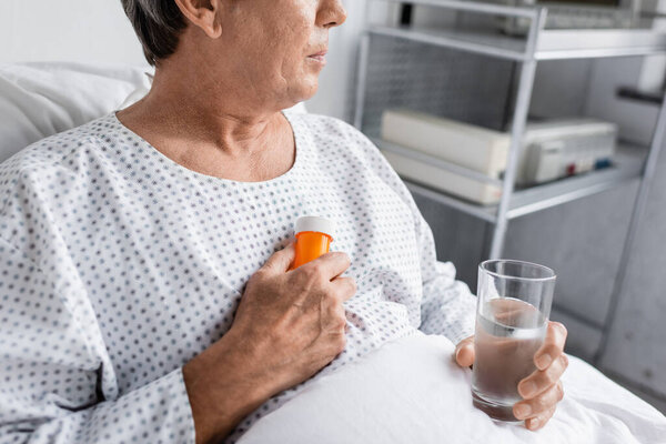 Cropped view of elderly patient holding pills and water in clinic