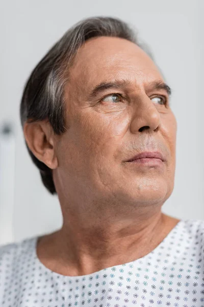 stock image Senior man in patient gown looking away in hospital ward