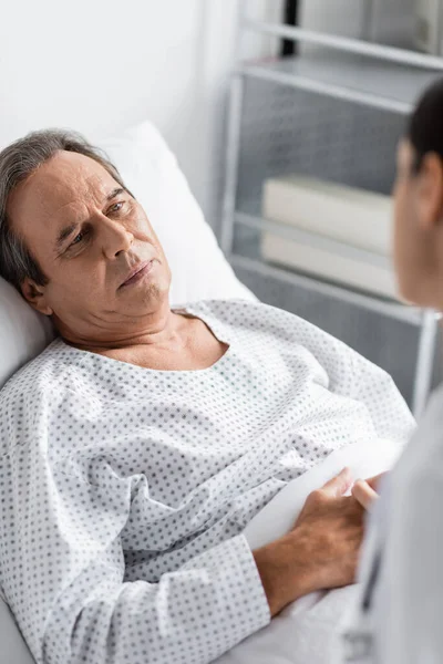 stock image Upset elderly patient looking at blurred doctor in hospital ward 