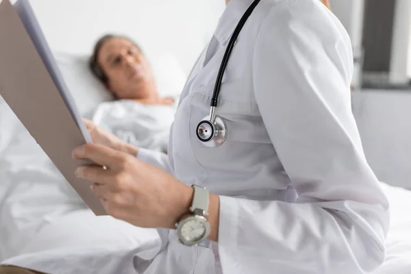 Beyaz Önlüklü Doktor Hastane Koğuşunda Bulanık Bir Hastanın Yanında Kağıt — Stok fotoğraf