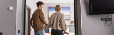 back view of young couple holding hands in hotel apartments, banner