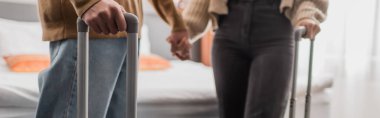 partial view of blurred couple holding hands in hotel room, banner