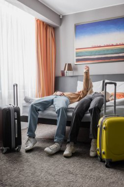 young couple of travelers holding hands and showing triumph gesture near suitcases in hotel bedroom clipart