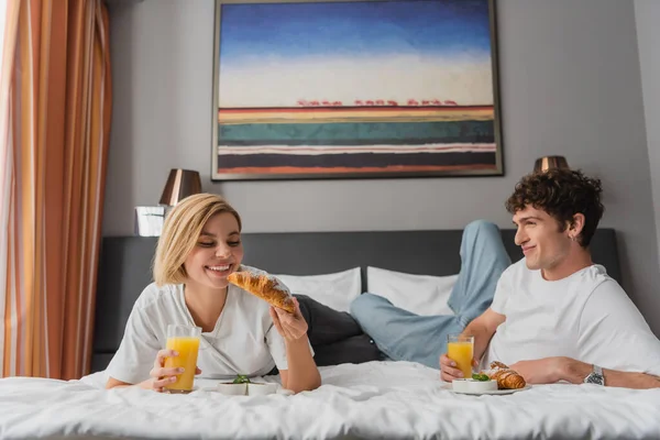 stock image pleased couple having breakfast with orange juice and croissants in modern hotel bedroom