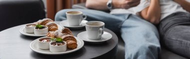 tasty croissants with jam and chocolate paste near coffee cups and cropped couple on blurred background, banner