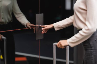 partial view of woman standing near reflective doors of elevator and pressing call button