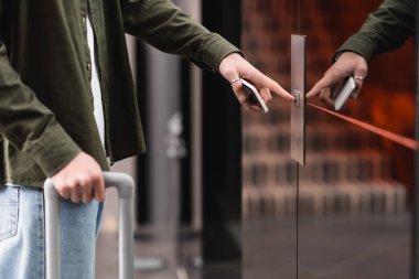 cropped view of man with mobile phone pressing elevator call button in hotel