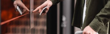 cropped view of man holding mobile phone and pressing call button of elevator in hotel, banner 