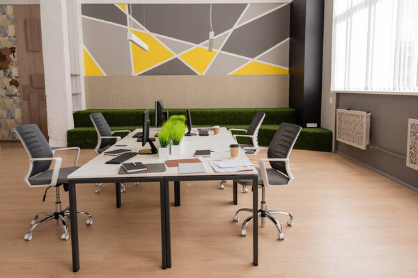 desk with computer monitors near documents and disposable cups in modern and spacious office