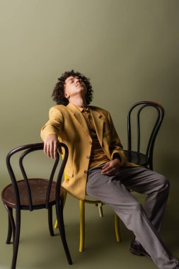 Genç ve modaya uygun Afro-Amerikalı gözleri kapalı zeytinli arka planda siyah sandalyelerin yanında oturuyor.