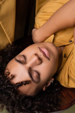 Sarı polo gömlekli, gözleri kapalı kıvırcık Afrikalı Amerikalı bir adam.