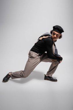 Siyah kazaklı, ekose atkılı, bereli, poz veren ve gri arka planda başka yöne bakan Afro-Amerikan bir adam.