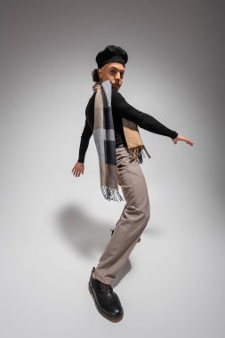 Gri arka planda poz verirken kameraya bakan siyah bereli ve kareli eşarplı Afro-Amerikan bir adam.