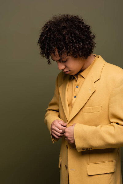 брюнетка африканский американец мужчина застегивая желтый пиджак на оливково-сером фоне