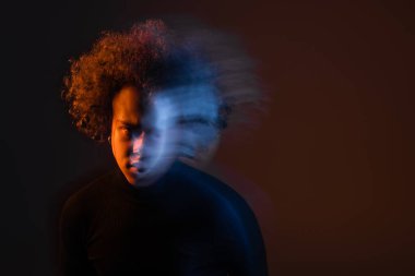 Uzun süre baskı altında kalan, bipolar bozukluğu olan, koyu renk arka planda turuncu ve mavi ışıkla kanayan Afro-Amerikan bir adam.