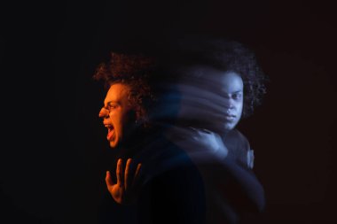 Çift taraflı depresif ve sinirli Afro-Amerikalı adam karanlıkta turuncu ve mavi ışıkla bağırıyor.
