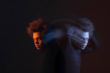double exposure of injured african american man with bipolar disorder looking at camera on dark background with orange and blue light clipart