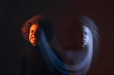 Çift taraflı Afro-Amerikan adam bipolar bozukluğu ve yaralı yüzü siyah arka planda turuncu ve mavi ışıkla ekşitme