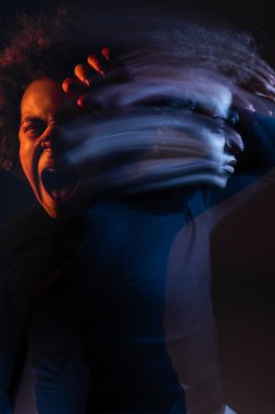 double exposure of irritated african american man with bipolar disorder screaming on dark background with orange and blue light clipart