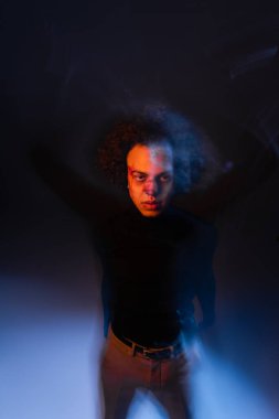 Yaralı Afro-Amerikalı, bipolar bozukluğu ve kanaması olan bir adam. Arka planda turuncu ve mavi ışıkla kameraya bakıyor.