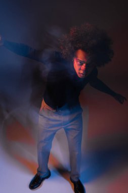 Yaralı Afro-Amerikalı yaralı bir adamın yüksek açılı görüntüsü. Yüzü kanayan bir adam. Arka planda koyu kırmızı ve mavi renkli kameraya bakıyor.