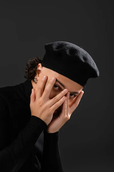 young african american man in trendy beret obscuring face with hands and looking at camera isolated on black