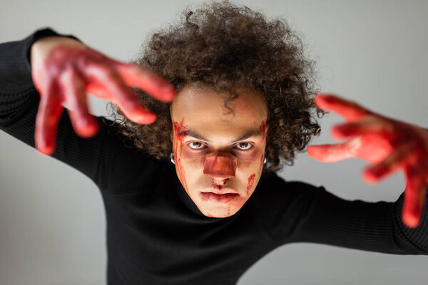 Африканский американец с раненым лицом и окровавленными руками, смотрящий в камеру, изолированную на сером