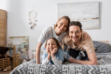 portrait of happy parents and kid looking at camera while resting in bedroom 