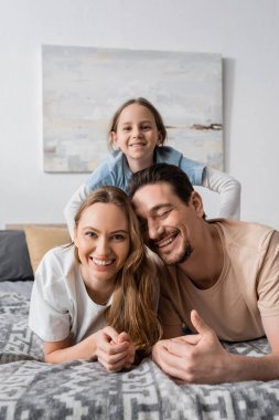 portrait of happy child behind cheerful parents resting in bedroom 