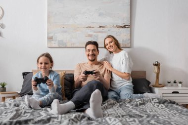 KYIV, UKRAINE - NOVEMBER 28, 2022: cheerful woman hugging husband playing video game with daughter 