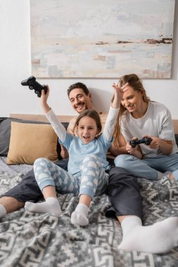 KYIV, UKRAINE - NOVEMBER 28, 2022: cheerful mother and excited child playing video game in bedroom 